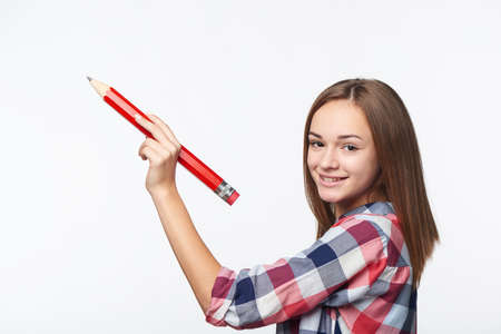 Smiling teen girl writing with big pencil on blank copy space looking at cameraの写真素材