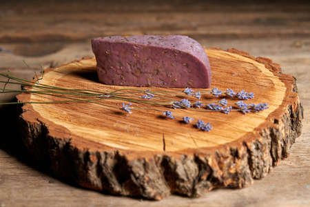 A piece of lavender cheese with twigs of fresh lavender flowers on rough wooden tree saw cutの写真素材