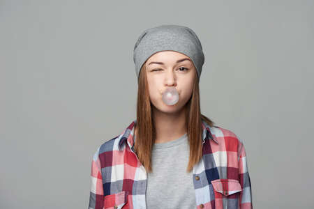 Closeup of teen girl blowing bubblegum winking at camera, studio portraitの写真素材