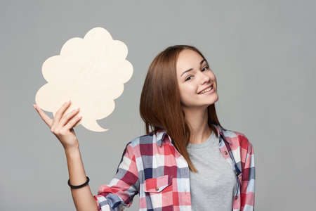 Smiling girl holding thinking bubble looking at camera, studio portraitの写真素材