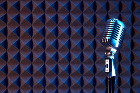 Studio retro condenser microphone on acoustic foam panel background with blue side lightの写真素材