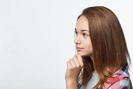 Profile portrait of thinking girl looking forward at blank copy space with hand on chinの写真素材