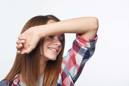 Smiling girl with raised hand shielding eyes, studio portraitの写真素材