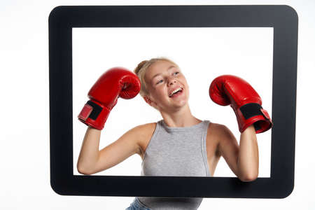 Internet battle winner concept. A girl wearing boxing gloves through digital tablet frame feeling triumphantの写真素材