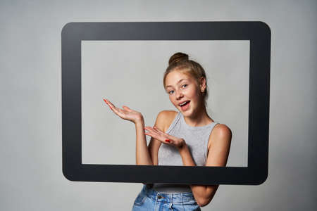 Happy excited teen girl looking through digital tablet frame and showing directing to blank copy...