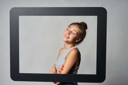 Lovely girl standing behind digital tablet frame smiling enjoying with closed eyesの写真素材
