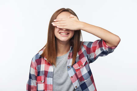 Emotional joyful teen girl covering her eyes with palm, studio portraitの写真素材