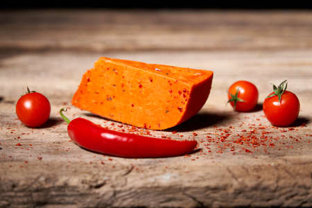 Red gourmet cheese with tomatos and parika on rough wooden planksの写真素材