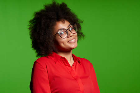 Closeup of smiling young African-American girl in glasses and red shirt looking at camera over green backgroundの写真素材