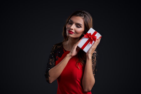 Gorgeous woman with red lipstick makeup holding gift box near her earの写真素材