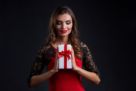 Gorgeous woman with red lipstick makeup holding gift box with red ribbonの写真素材