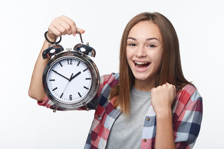 Happy excited winning successful teen girl holding big alarm clock screaming, isolated over white background. Time conceptの写真素材