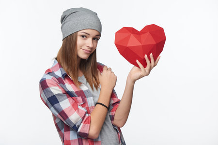 Smiling girl holding red polygonal paper heart shape, studio portraitの写真素材