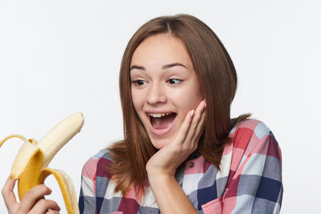 Closeup of happy surprised teen girl holding half peeled banana shoutingの写真素材