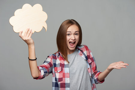 Indignant female holding thinking bubble and screaming, over grey backgroundの写真素材