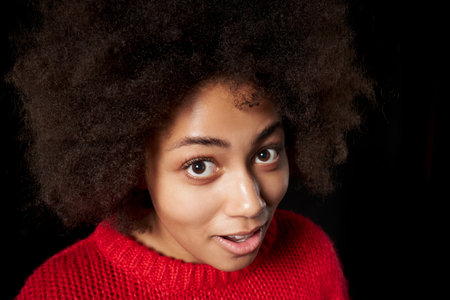 Curious surprised smiling mixed race African-Caucasian girl peeking in camera, over black background. Wide angle portraitの写真素材