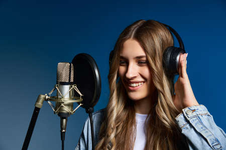 Girl blogger recording audio podcast. Happy smiling girl with microphone with headphone on her headの写真素材