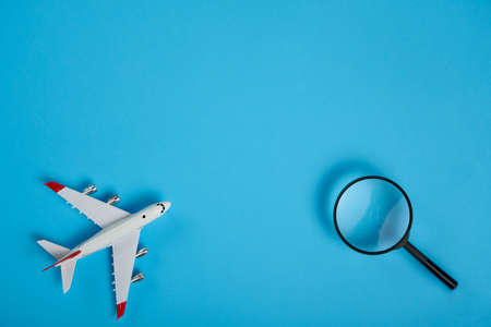 Airplane tickets search concept. Small souvenir aeroplane with magnifying glass over blue backgroundの写真素材
