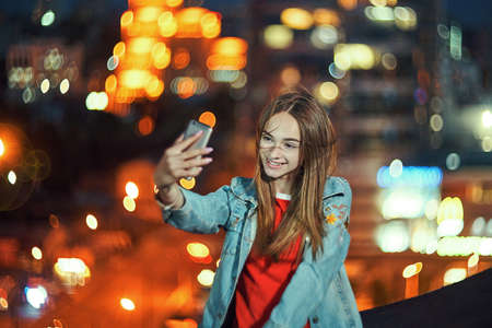 Teen girl on cityscape background making self portrait with her smart phoneの写真素材