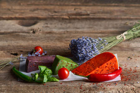 Three different colored gourmet cheeses lying on rough wooden planks with vegetables, copy space aboveの写真素材