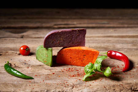 Three different colored gourmet cheeses lying on rough wooden planks with vegetables, copy space aboveの写真素材