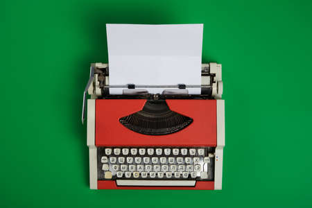 Top view of red vintage typewriter with white blank paper sheet on green background. Horizontal.の写真素材