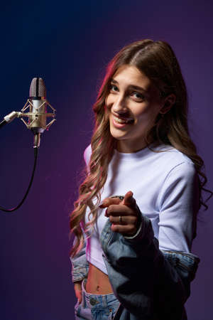 Girl blogger recording audio podcast. Happy smiling girl with microphone pointing at camera at youの写真素材