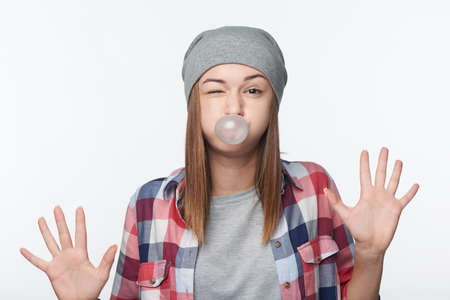 Fooling teen girl blowing bubblegum showing palms, winking, studio portrait over white backgroundの写真素材