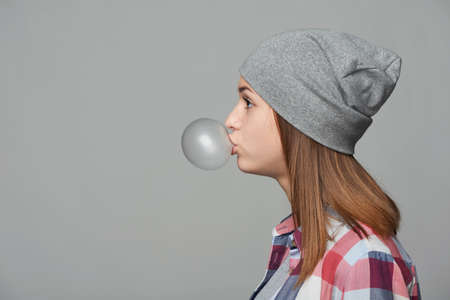 Profile closeup portrait of teen girl blowing bubblegum over grey backgroundの写真素材