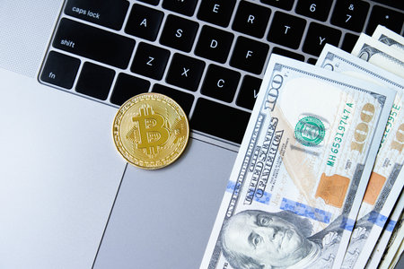 Golden bitcoin coin and US dollars on laptop keyboardの写真素材