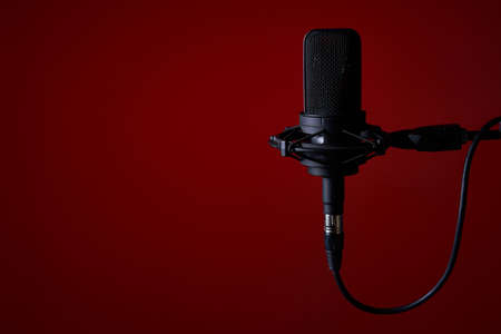 Black studio condenser microphone on red background, with copy space on leftの写真素材