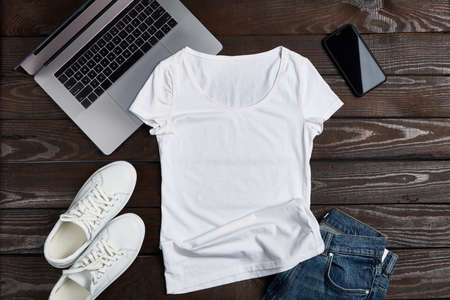 T-shirt mockup. Flat lay of white t-shirt lying on rough wooden planks with laptop, smartphone and apparel accessories.の写真素材