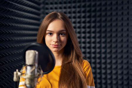 Teen girl in recording studio with mic over acoustic panel backgroundの写真素材