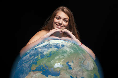 Woman with earth globe gesturing heart shape with fingersの写真素材