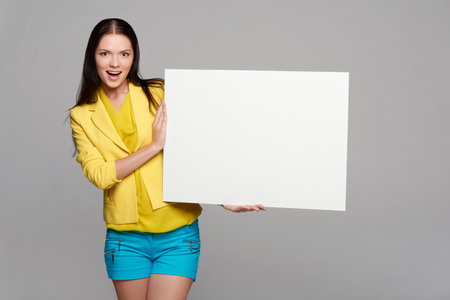 Happy excited girl in yellow and blue, holding empty whiteboardの写真素材