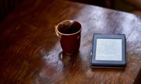 E-book lying on rural weathered wooden table with ceramic tea cupの写真素材