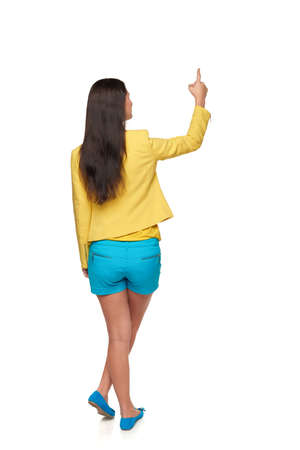 Back view of young casual female in full length pointing at blank copy space, isolated on whiteの写真素材