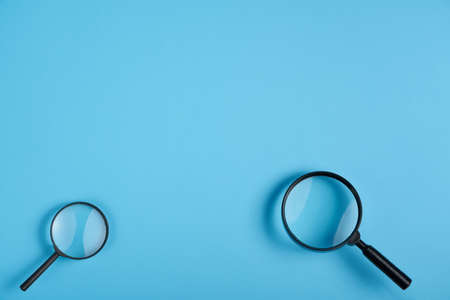 Two magnifying glass big and small lying on blue background, top view with negative space aboveの写真素材