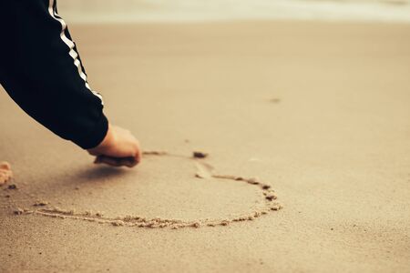 Girl at the beach drawing hearts on a sand.  love concept. Selective focusの写真素材