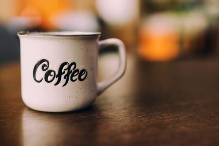 Enamel white metal mug with  inscription  coffee on  wooden table on blurred background. White cup of coffee on a dark background. Place for text or advertisingの写真素材
