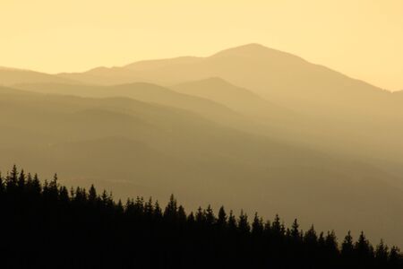 Warm gradient of dawn sky above layers of mountain and rock silhouettes. Vivid alpine landscape with dark rockies and orange sunrise sky. Minimalist highland scenery with silhouette of rocky mountainsの写真素材