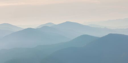 Warm gradient of dawn sky above layers of mountain and rock silhouettes. Vivid alpine landscape with dark rockies and orange sunrise sky. Minimalist highland scenery with silhouette of rocky mountains の写真素材