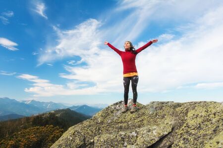 The young girl  at the top of the mountain raised her hands up on blue sky background. The woman...