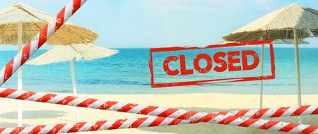 Red inscription "closed" on a blurred background of a deserted beach. Beach is closed with a  red barrier tape. Concept: vacation canceled due Covid-19, resort closing due to quarantineの写真素材