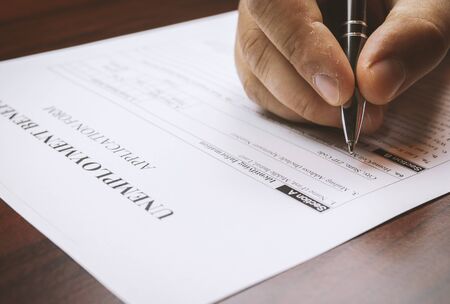 Close-up of a person's hand filing social security benefits application form.
