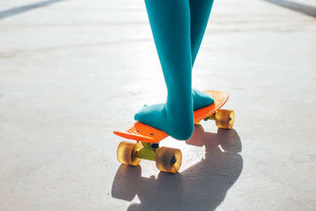 Close-up of female young girl legs in green socks standing on a orange plastic skateboard. Summer sports activities for teens, active kids lifestyle. socks advertising conceptの写真素材