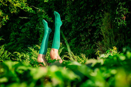 Girl lies in the grass with her legs up in green socks. Legs stick out in the field at green vegetation background. socks advertising concept. Selective focus, extremely shallow DOF.の写真素材