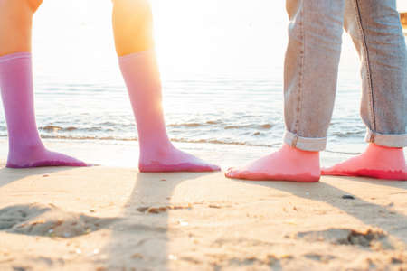two girls stand on the beach in socks on their bare feet. close-up at sunrise. socks advertising conceptの写真素材