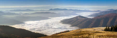 Panorama alpine landscape of the mountain peaks and valleys covered in fog at dawn. Autumn landscape mountains and colorful forest on background sunrise.の写真素材