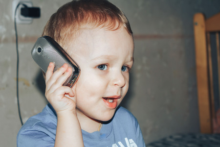 little boy is calling on the phone at homeの写真素材